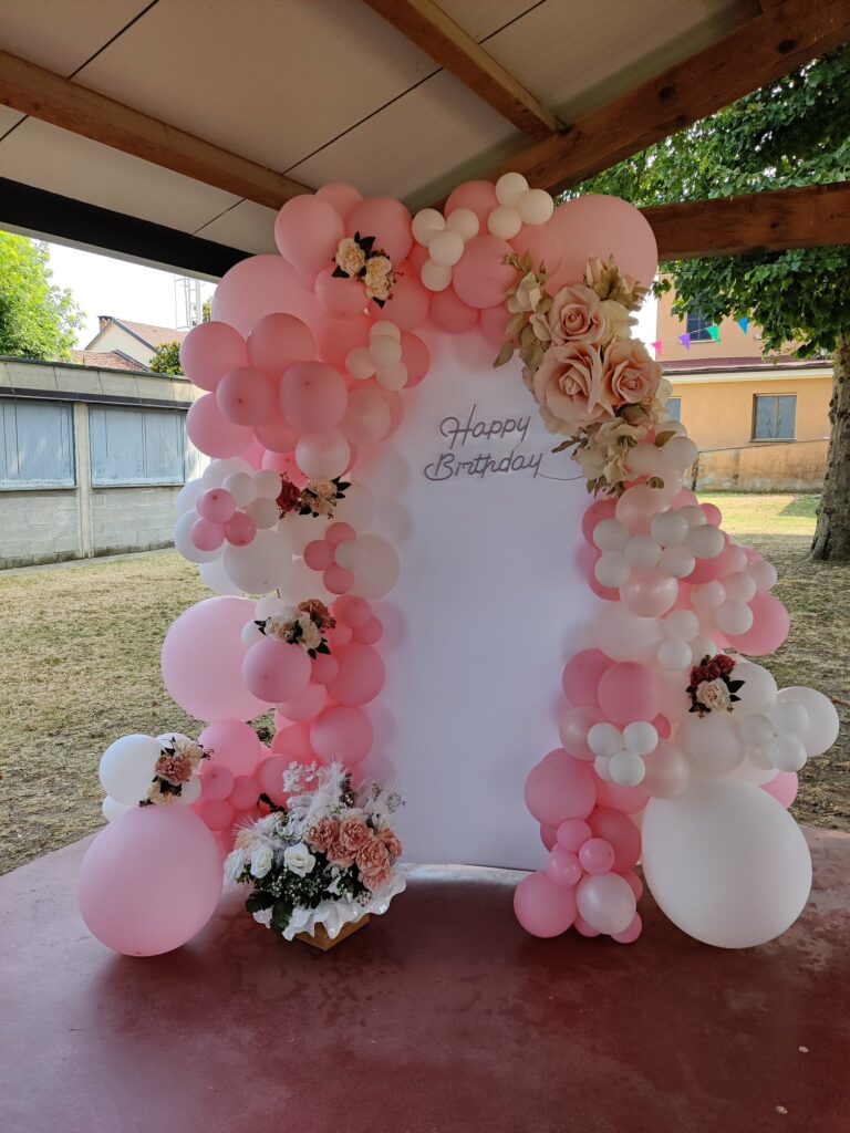 Fotografia di una zona compleanno con palloncini rosa e bianchi, fiori e pannello Happy Birthday